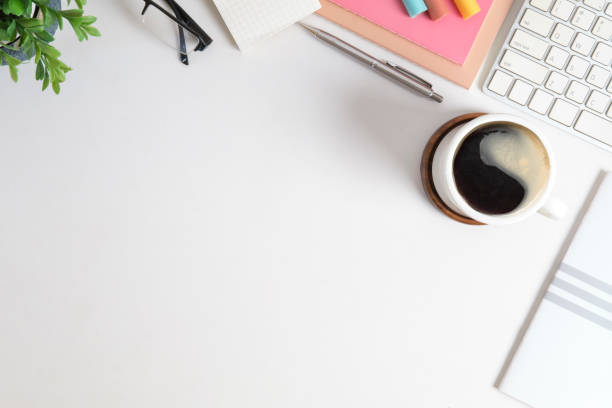 istock Feminine workplace, coffee cup, notepad, glasses, and potted plant on white table. Top view with copy space for your text. 1454406047