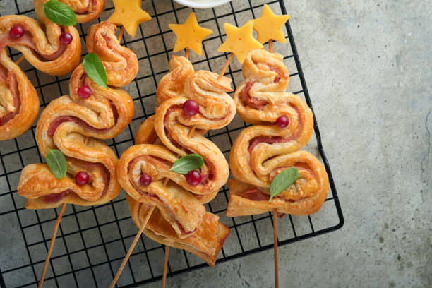 Christmas or New Year appetizer. Christmas tree shape puff pastry buns with cheese and ham. Group of Christmas tree shapes on stand for hot. Festive idea for Christmas or New Year dinner. Top view.