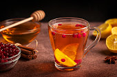 Herbal healthy vitamin hot tea with lemon slices, berries and honey served in glass cup on dark brown table in winter