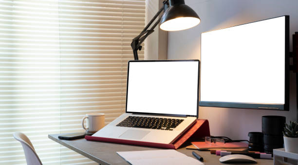 istock Modern workplace with white blank computer screen, laptop and supplies on black table. 1454408436