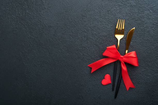 istock Valentines day romantic table setting. Empty or closeup of a dinner black plate, knife, fork and decorative silk hearts on black background. Holiday concept. Copy space for inscriptions. 1454408885