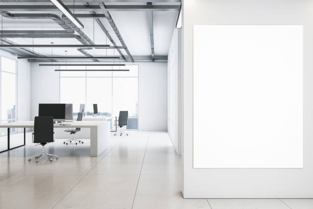 istock Front view on blank white poster on light wall background in spacious coworking office with monochrome interior design, light glossy floor, loft ceiling lamps and big window. 3D rendering, mock up 1454410101