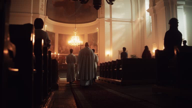 Liturgy in Grand Church: Majestic Procession Of Priests Walking with Processional Cross to Altar. Congregation Stands In Reverence, Christians Rejoice In Mass Ceremony. Slow Motion Back View