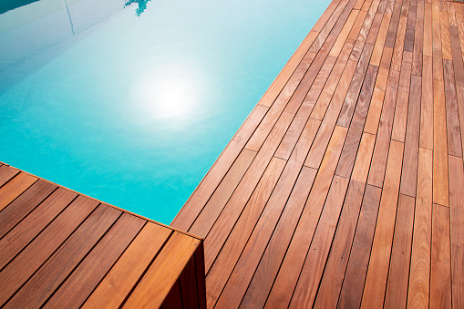 Texture with tiled wooden decorative planking, hardwood ipe pool deck shining sun reflecting on the water