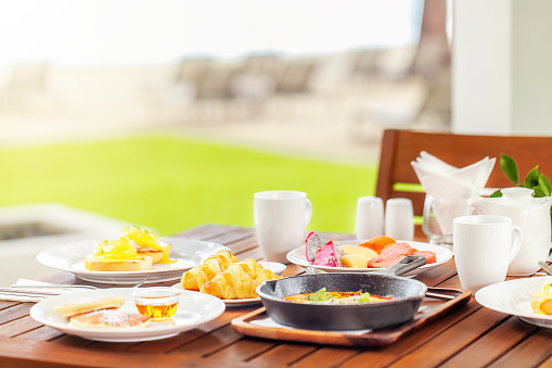 Healthy breakfast in outdoors cafe. Fresh bakery on plate on the wooden table full of various colorful food on lunch time - eggs Benedict, Shakshuka, tropical fruits. Hotel morning.