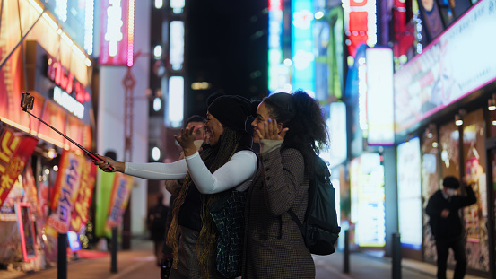 A multi-racial group of tourist friends are taking selfies and videos while exploring the city In Tokyo at night.