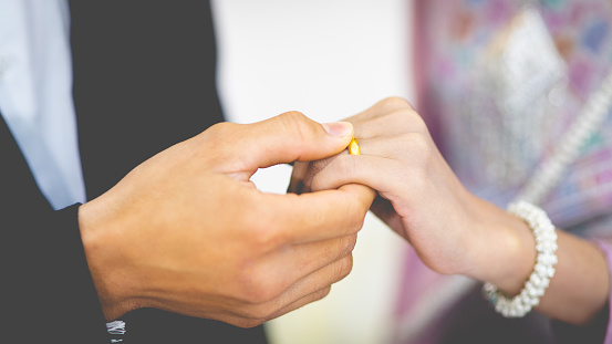 A groom puts a wedding ring on the bride finger