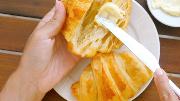 kobiece ręce kroją nożem świeżego rogalika i rozprowadzają masło - french toast toast butter breakfast zdjęcia i obrazy z banku zdjęć
