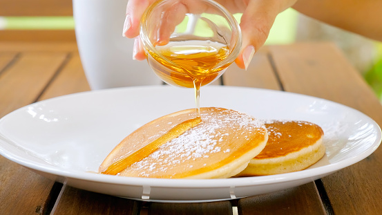 Woman hands pouring maple syrup on buttermilk pancakes. Close up of traditional American morning breakfast with sweet fluffy tasty pancakes.