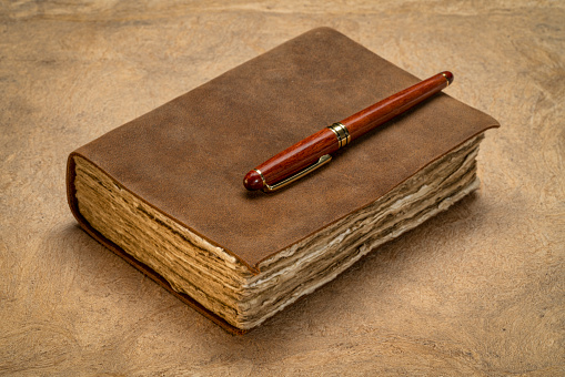 retro leather-bound journal with decked edge handmade paper pages and a stylish pen on a textured bark paper, journaling concept