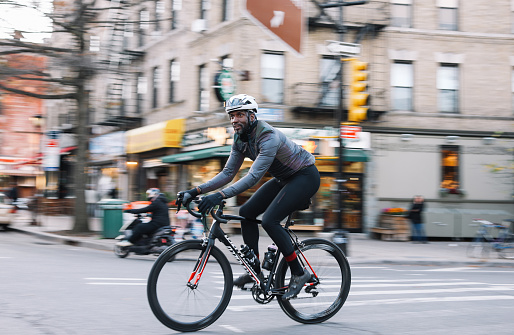Black male cyclist riding through Brooklyn, New York. He is wearing cycling gear, going for a training ride or commuting in style, on a sunny Autumn day.