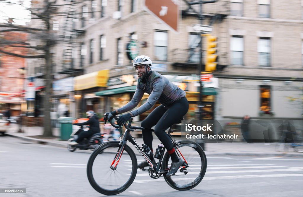 cycling fast through Brooklyn, NYC Black male cyclist riding through Brooklyn, New York. He is wearing cycling gear, going for a training ride or commuting in style, on a sunny Autumn day. Cycling Stock Photo