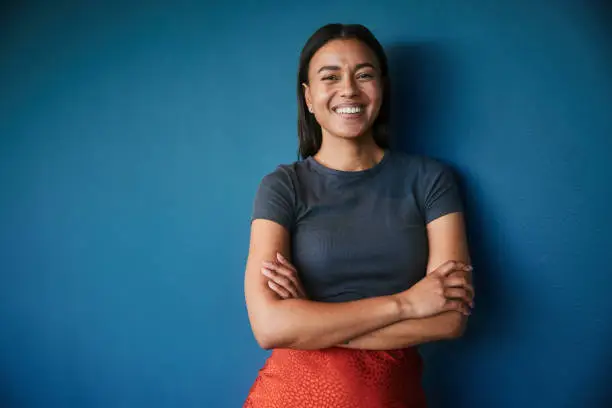 Portrait of a young businesswoman smiling while standing with her arms crossed against a blue background