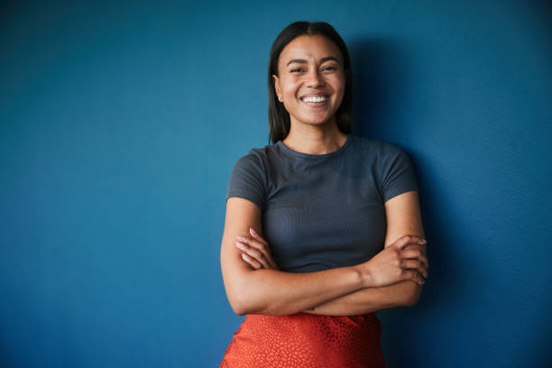 jovem empresária sorrindo enquanto está de pé contra um pano de fundo azul - portrait women laughing black - fotografias e filmes do acervo