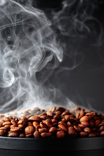 Steaming coffee beans on a black background. Selective focus. Copy space.