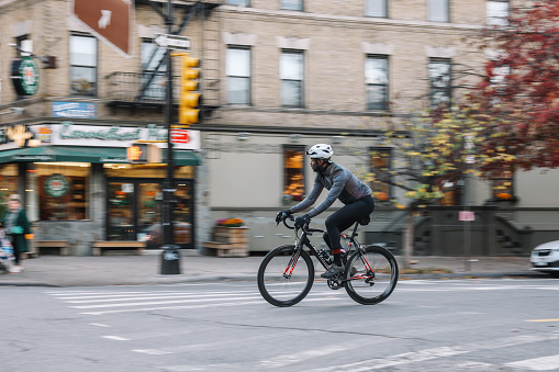 Black male cyclist riding through Brooklyn, New York. He is wearing cycling gear, going for a training ride or commuting in style, on a sunny Autumn day.