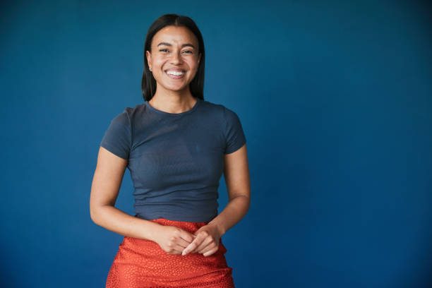 smiling young businesswoman standing in front of a blue backdrop - seri bölümü stok fotoğraflar ve resimler