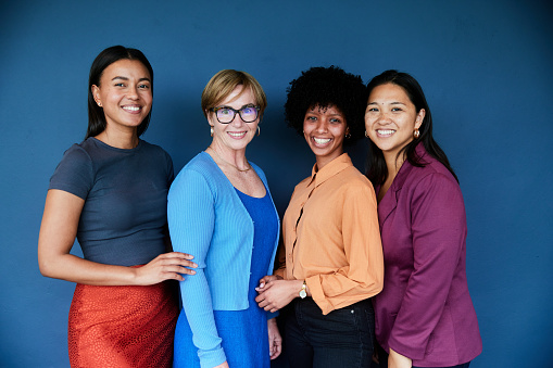 Portrait of a diverse group of smiling businesswomen standing together in front of a blue background