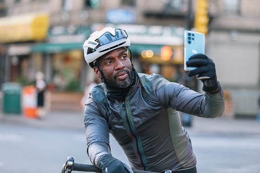 Black male cyclist riding through Brooklyn, New York. He is stopping to check messages or ride route on his smartphone.