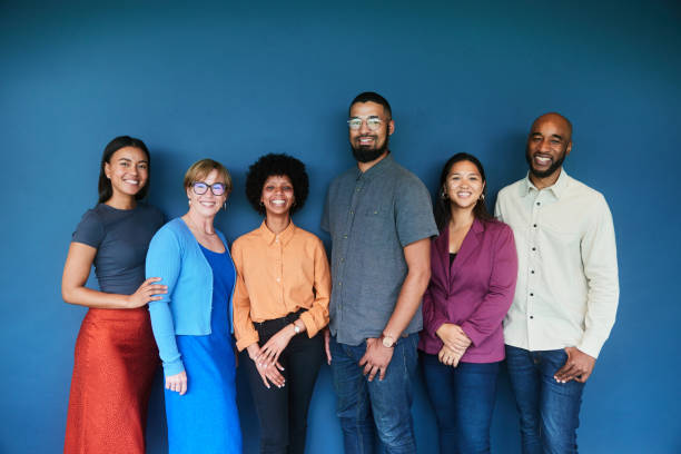 Smiling group of diverse businesspeople standing against a blue background Portrait of a diverse group of smiling businesspeople standing together in front of a blue background studio workplace stock pictures, royalty-free photos & images