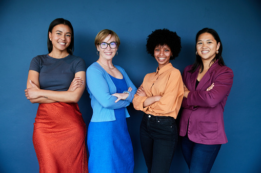 Portrait of a smiling group of diverse businesswomen standing together in front of a blue background
