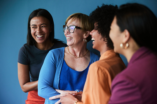 Group of diverse businesswomen laughing while standing together in front of a blue background