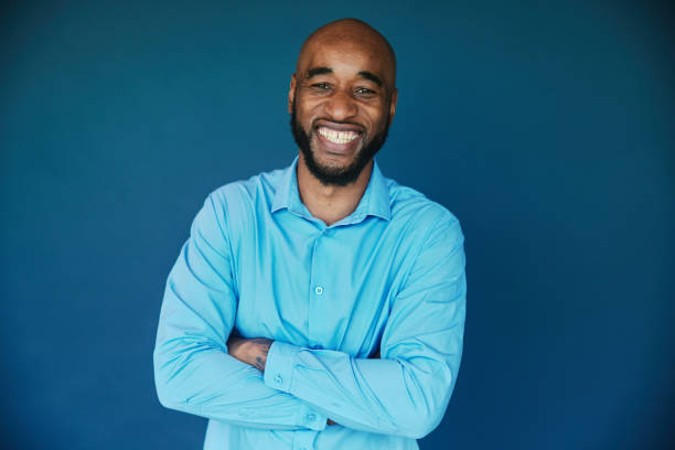 istock Businessman smiling while standing with his arms crossed on a blue backdrop 1454423798