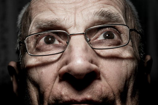 Head photo shot of old pensive man with wrinkled face wearing eyeglasses. Detail photography of senior male person in spectacles.