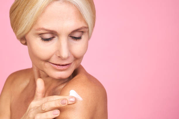 Close-up, pretty mature blonde woman applying cream on her body. stock photo