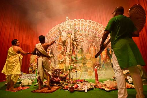 Howrah, India -October 13, 2021 : Hindu Priests worshipping Goddess Durga with panchapradip, ghanta, chamor and hand fan. Ashtami puja aarati - sacred Durga Puja ritual - shot at night.
