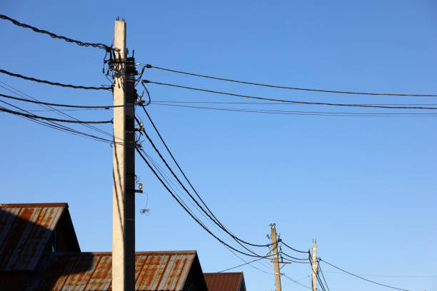 istock Powerline posts with electrical wires and capacitors above old roofs on blue sky background 1454426806