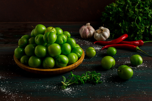 Tkemali, green cherry plum, with ingredients for sauce, cilantro, mint, hot pepper, garlic, on a wooden table, close-up, rustic, food background, no people, selective focus,