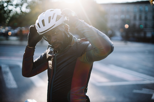Black male cyclist riding through Brooklyn, New York. He is preparing for the ride, setting up his cycling gear, going for a training ride or commuting in style, on a sunny Autumn day.