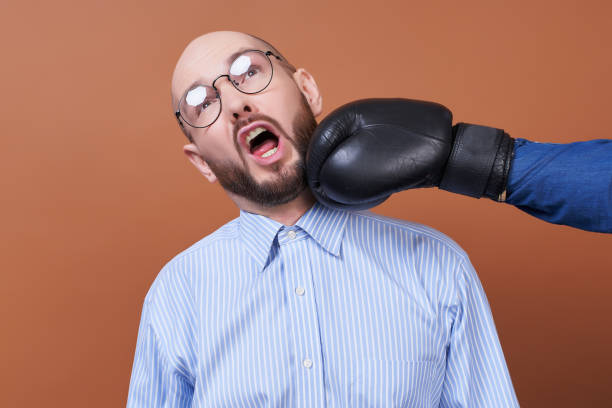 A nerd in round glasses hits his face with a boxer glove. stock photo