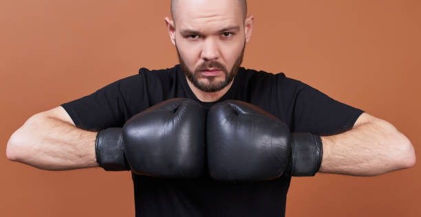 Close-up, a boxer in gloves seriously looks right at the brown background. stock photo