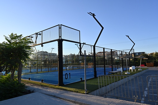 Ammourdara, Greece, 09 20 2022: An enclosed blue court for padel with construction created by mesh and the glass back walls. Padel is a racket sport played in doubles and is similar to tennis with the same rules of scoring.