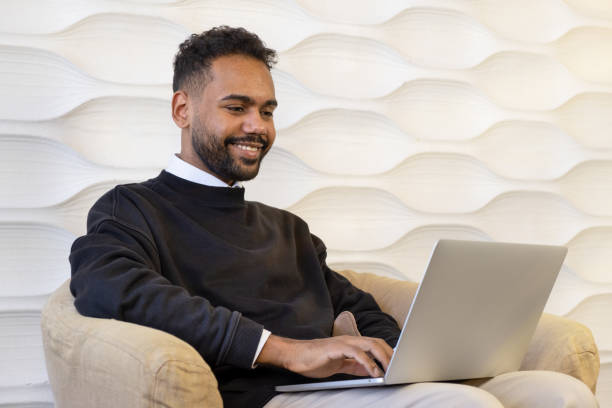 earded young man using laptop, sitting on couch at home, handsome guy having video call online in social network, having fun, watching movie, freelancer working on computer project
