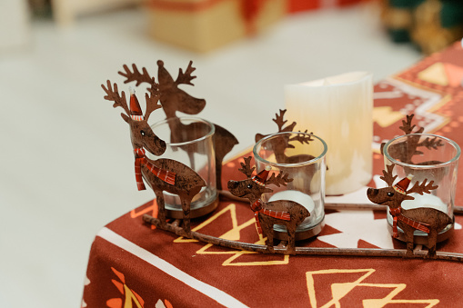 Close up of Christmas decorations objects reindeer drinking glasses on table with candle inside the living room in house.

Festive scenes with Christmas objects in a Christmas party in living room at home indoors during winter holidays friend gathering or meet-up.