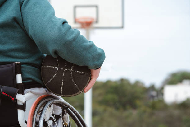 person using wheelchair holding ball under arm in basketball court outdoor