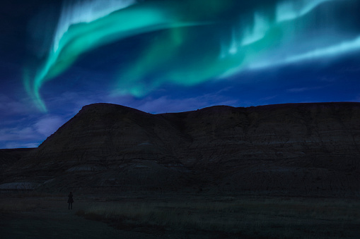A person admiring the Northern lights above the beautiful landscape of the Canadian Badlands in Drumheller, Alberta, Canada.
