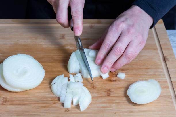istock Slightly blurred working woman's hands using a knife to cut onion on a wooden kitchen board. Food preparation concept. 1454447255