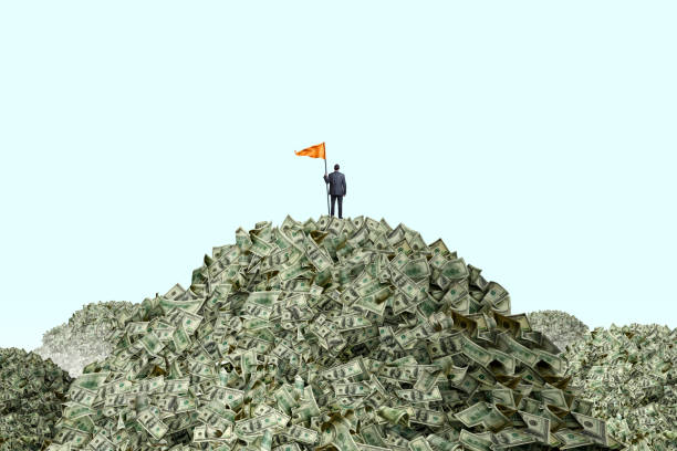 Man Planting Flag On Piles Of Cash A businessman stands at the top of a mountain of money as he holds a large orange flag attached to a pole. He stands with his back to the camera as he looks out into the distance towards other mountains of money that he has yet to conquer. greedy corporation stock pictures, royalty-free photos & images