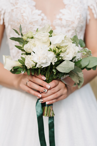 wedding bouquet of white roses in the hands of the bride on the background of dress