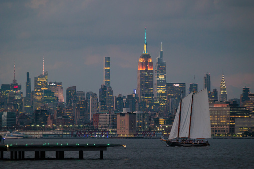 A sailing ship sails in front of the New York City Skyline on the Hudson River at Dusk