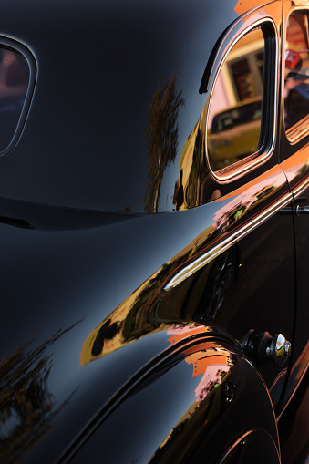 Vintage classic car in beautiful shiny black finish - shown from an angled rear view and cropped tightly.  In the vertical frame is shown most of the passenger side portion of the trunk and rear quarterpanel, including chrome side trim, the top of the rear fender and the rear side window.