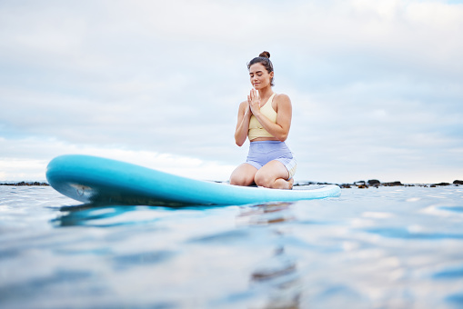 Yoga meditation, ocean and surfer woman meditating for health wellness, peace or freedom on sea water. Surfboard pilates, prayer and zen girl meditate for beach fitness, aura or chakra energy healing