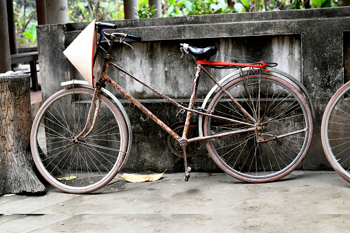 Old, and rusty bicycle parked beside a wall with a typical Vietnamese hat hanging, Vietnam.