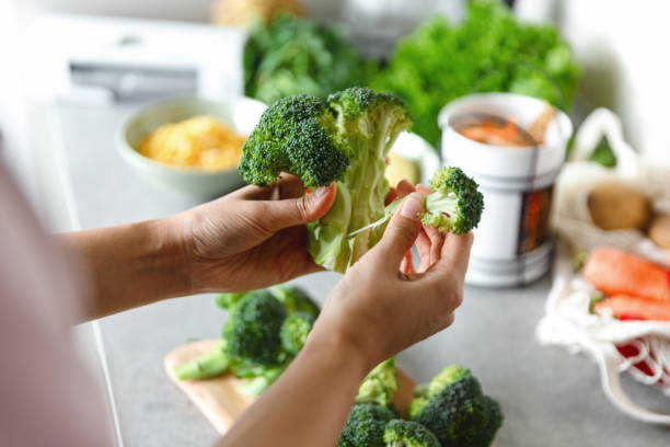 Woman's hand peeling broccoli Woman preparing healthy vegetarian food. Cutting vegetables into small pieces. broccoli stock pictures, royalty-free photos & images