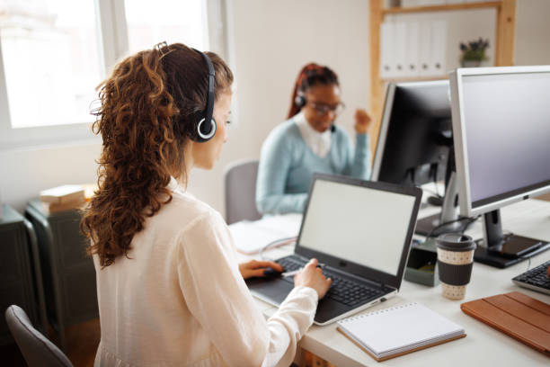 istock Call center agent with headset working on support hotline in modern office with her coworker 1454460625