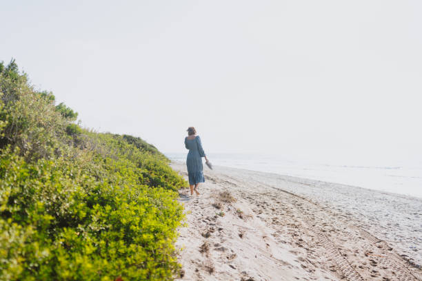 Practicing mindfulness Photo of a mid adult woman walking down the beach: taking care of herself, her mental and physical health walking beach women sadness stock pictures, royalty-free photos & images